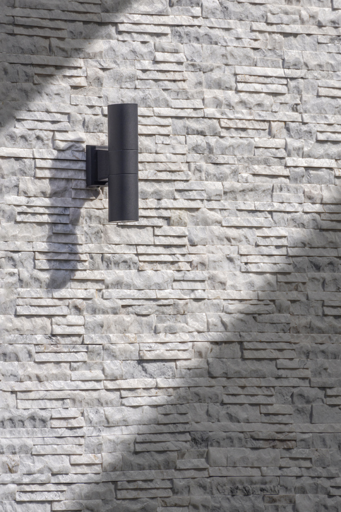 Sunlight and shadow on surface of outdoor black cylinder wall lamp on vintage white and gray ledgestone wall